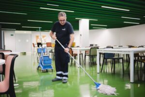 Empresa de limpieza de oficinas. Trabajador limpiando el suelo de una zona común de una oficina